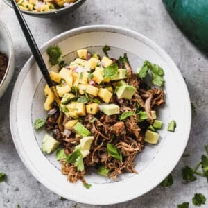 A mojo pork recipe on a bed of black beans and topped with fresh mango and cilantro.