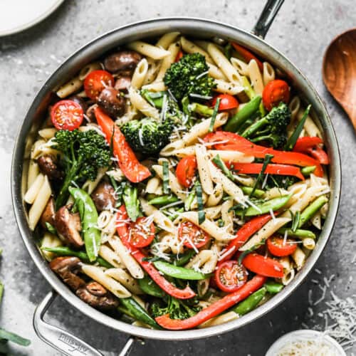 A creamy pasta primavera recipe in a large stainless steel pan, garnished with fresh basil, ready to serve.