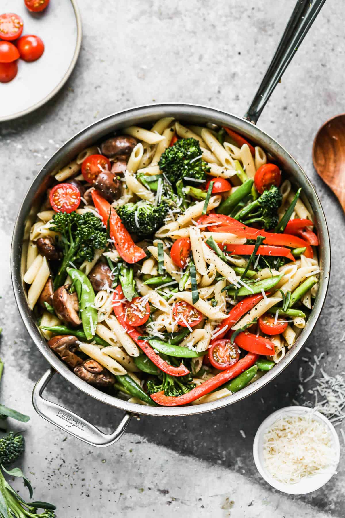 A creamy pasta primavera recipe in a large stainless steel pan, garnished with fresh basil, ready to serve.