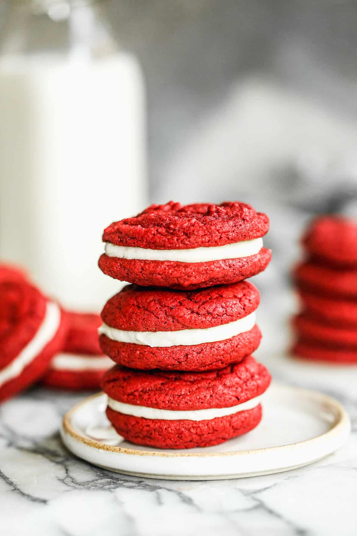 Three homemade red velvet cookies with cream cheese filling stacked on top of each other on a small plate.