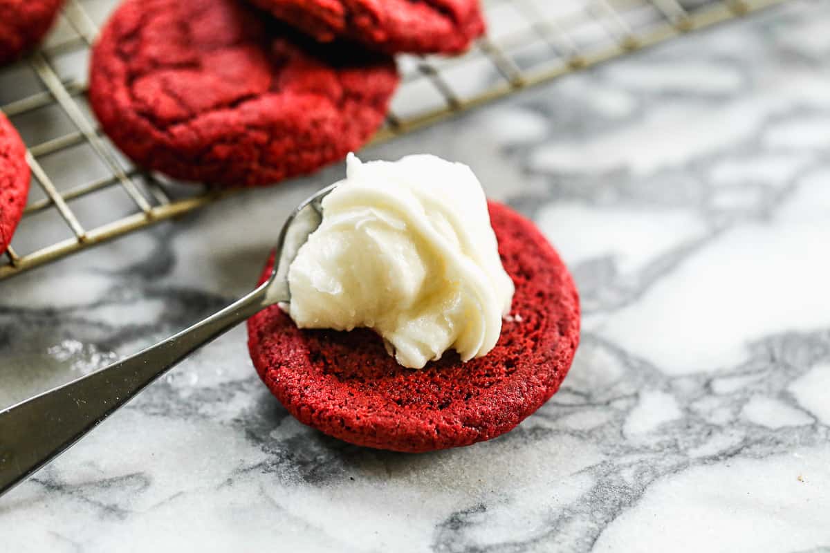 Red velvet cookies with cream cheese being spread before being sandwiched to make a red velvet oreo cookie.
