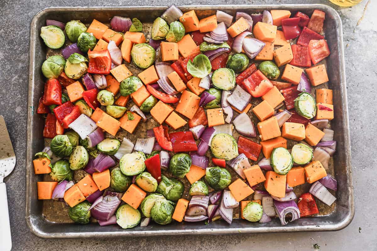 Chopped butternut squash, brussels sprouts, red onion, and red bell pepper on a baking sheet, ready for roasting. 