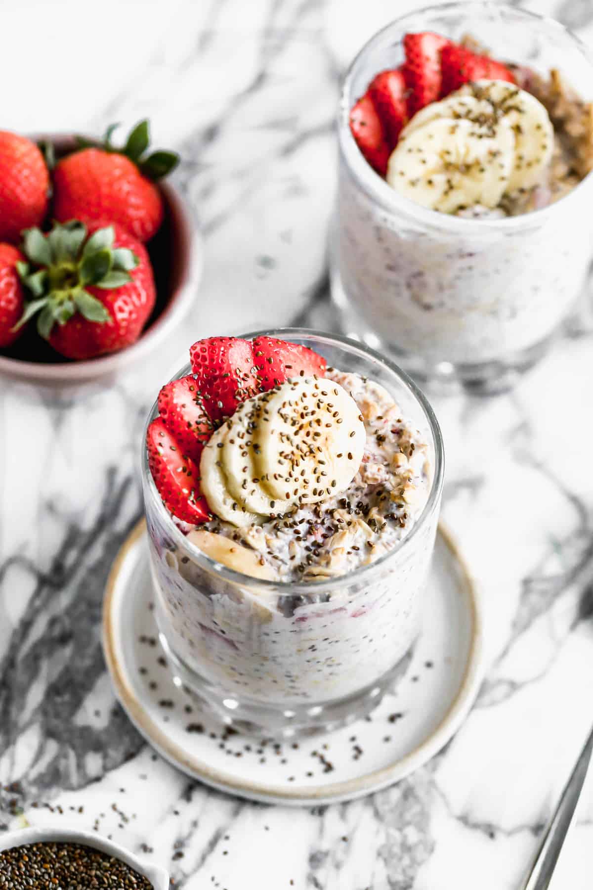 A glass of healthy Strawberry Overnight Oats recipe, topped with fresh sliced strawberries, bananas, and a sprinkle of chia seeds.
