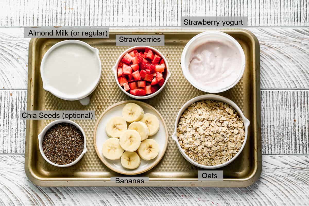 Everything you need to make strawberry banana overnight oats: milk, chia seeds, strawberry yogurt, oats, strawberries, and bananas.