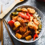 And easy Sweet and Sour Chicken recipe with peppers and pineapple, served in a bowl on a bed of steamed rice.
