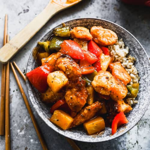 And easy Sweet and Sour Chicken recipe with peppers and pineapple, served in a bowl on a bed of steamed rice.