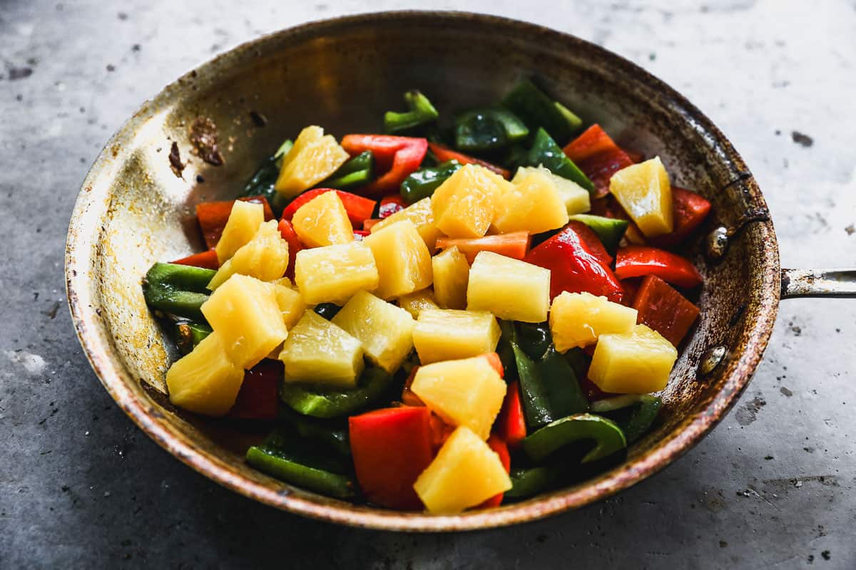 A frying pan filled with sautéed red and green bell peppers and pineapple on top.