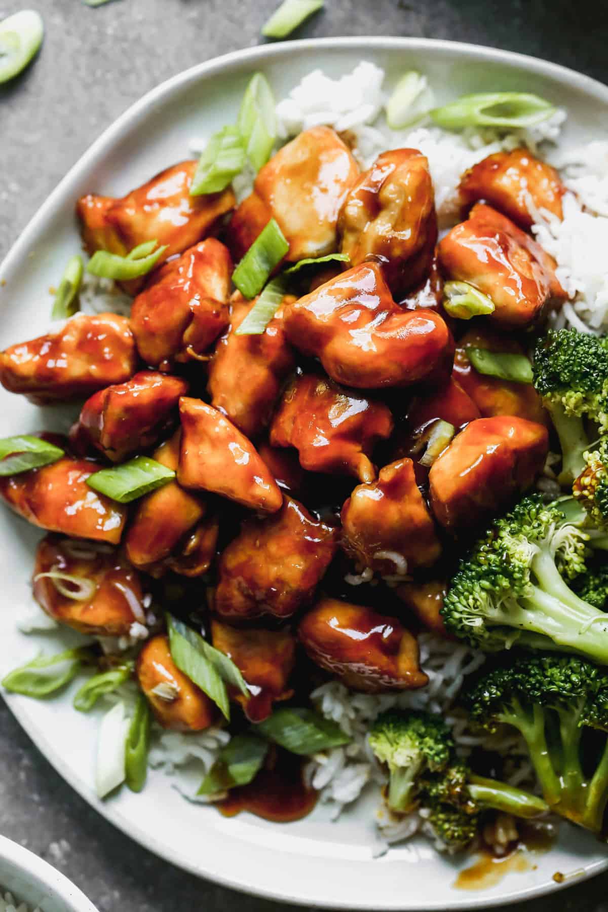 A close up image of quick teriyaki chicken on a bed of rice with steamed broccoli and garnished with green onions. 