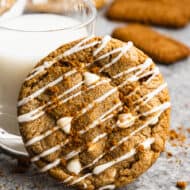 A lotus biscoff cookie with white chocolate chips, leaning against a glass of milk.