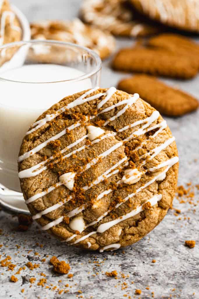A lotus biscoff cookie with white chocolate chips, leaning against a glass of milk.