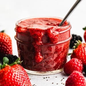 A strawberry Chia Seed Jam recipe in a jar with a spoon for serving, that can be made with any type of fruit!