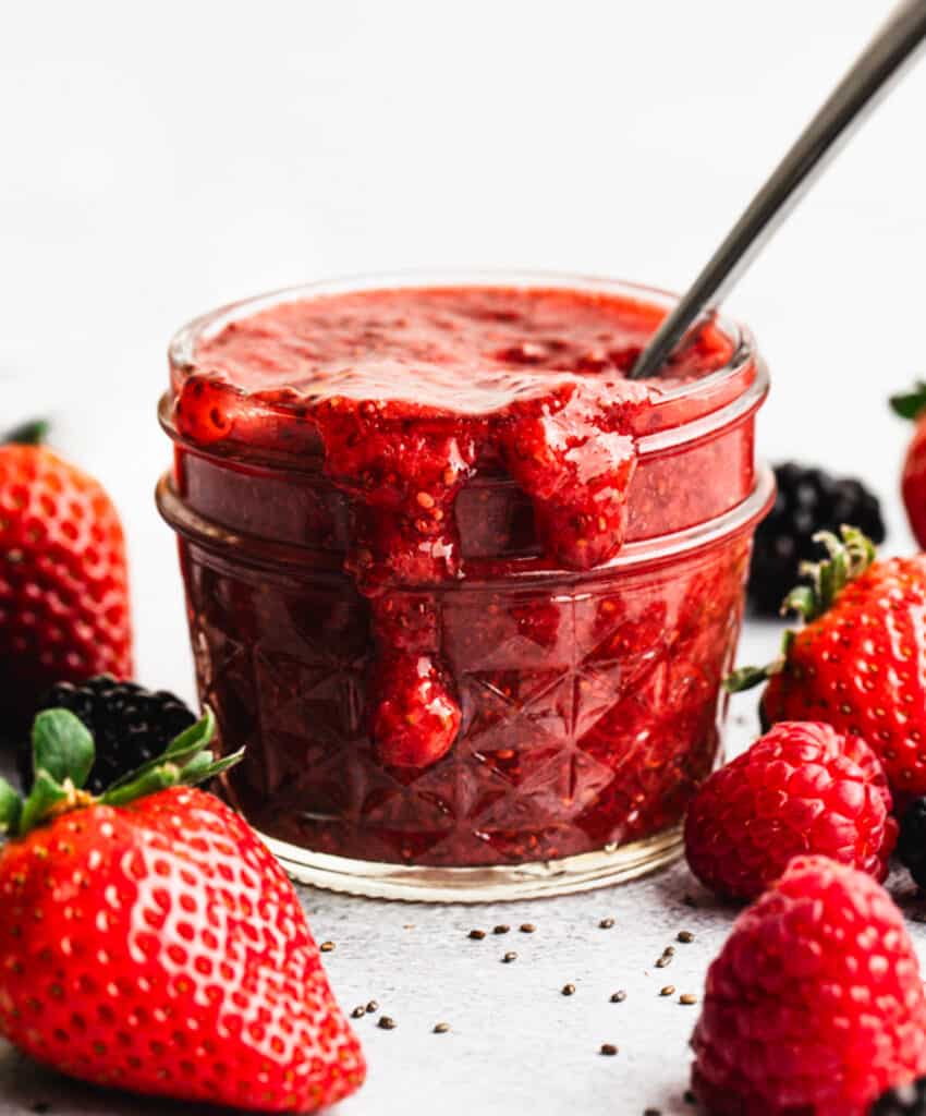 A strawberry Chia Seed Jam recipe in a jar with a spoon for serving, that can be made with any type of fruit!