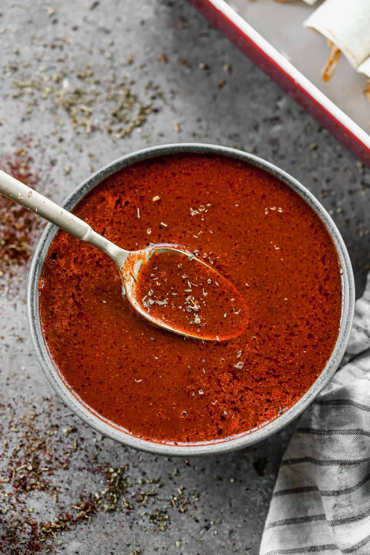 The best enchilada sauce recipe in a bowl with a spoon lifting some up, ready to be used in a recipe.