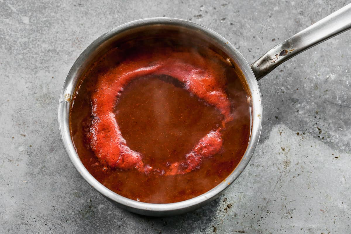 A quick enchilada sauce recipe simmering in a stainless steel pot on the stove.