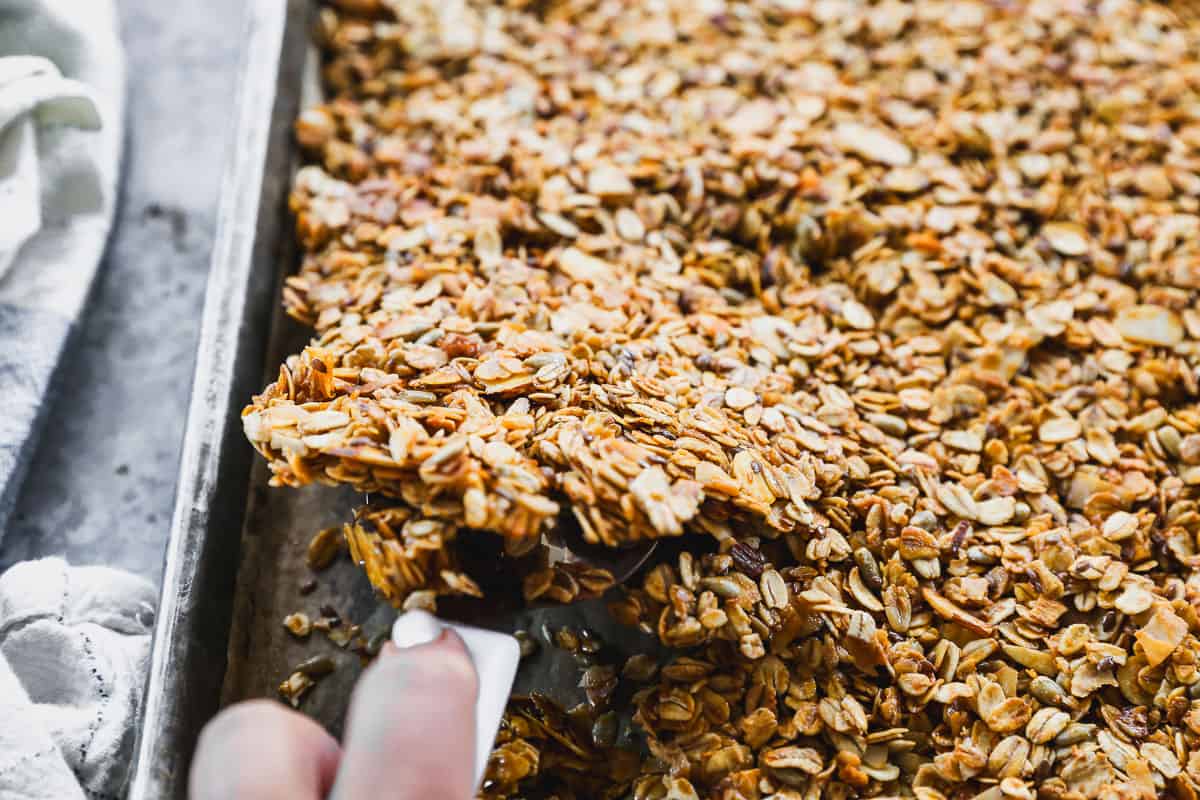 A healthy granola recipe being baked on a sheet pan, being flipped with a spatula.