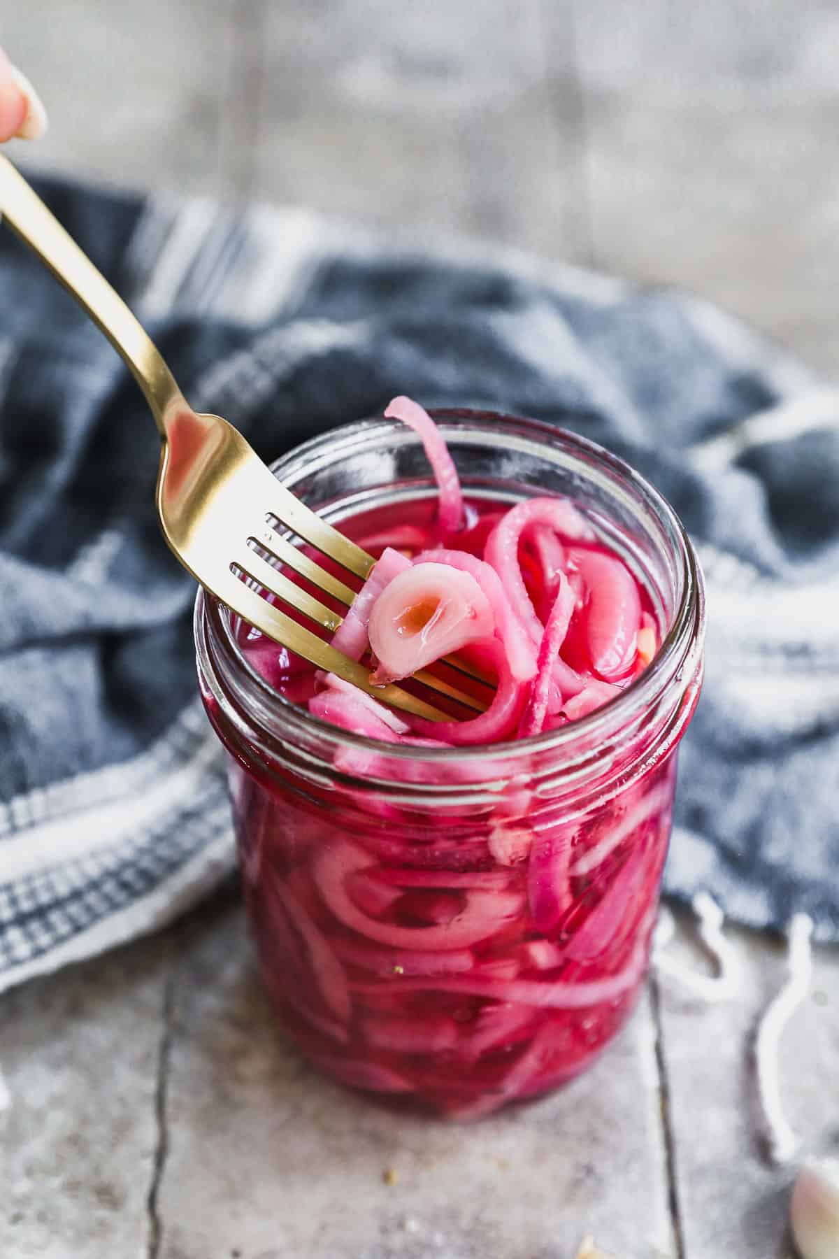 The best Pickled Red Onions recipe in a jar, some of it being picked up with a gold fork. 
