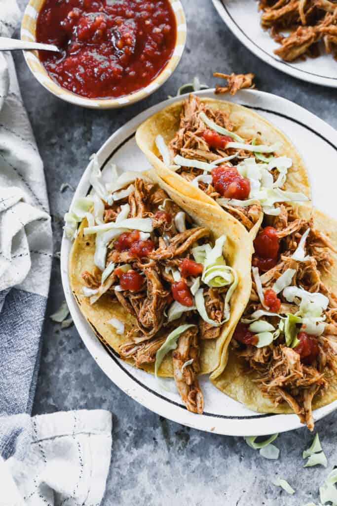 An easy slow cooker chicken tacos recipe in corn tortillas, topped with lettuce and salsa.