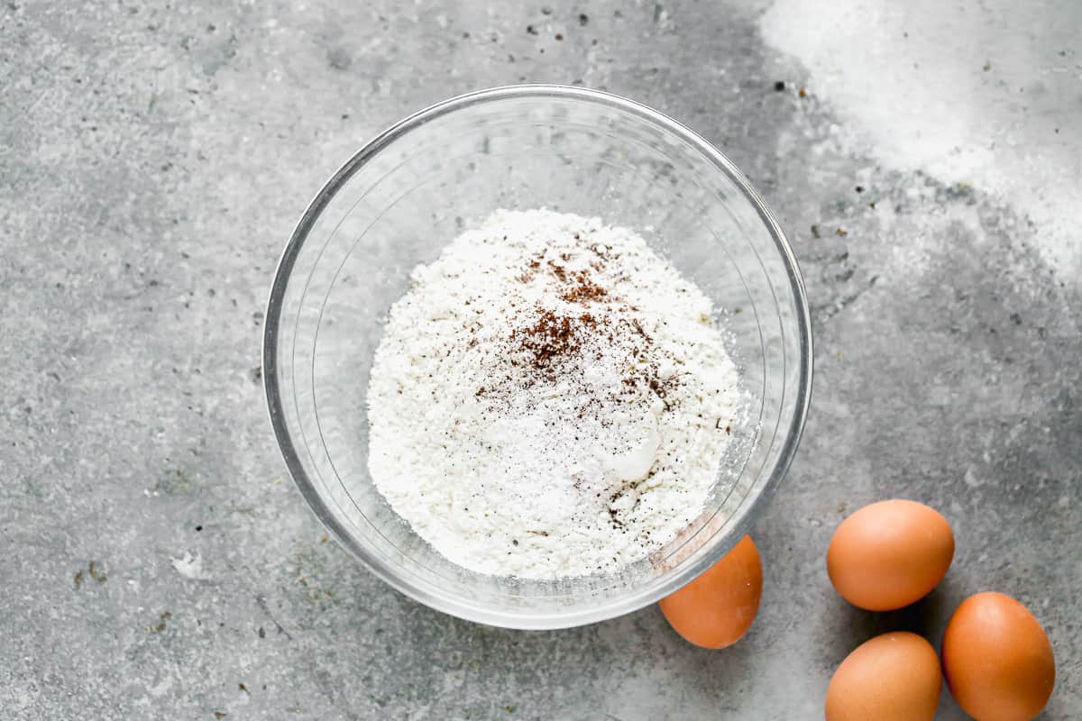 A glass mixing bowl with flour, salt, and nutmeg.