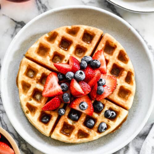 A plate with an overnight Yeasted Waffle topped with fresh strawberries and blueberries.