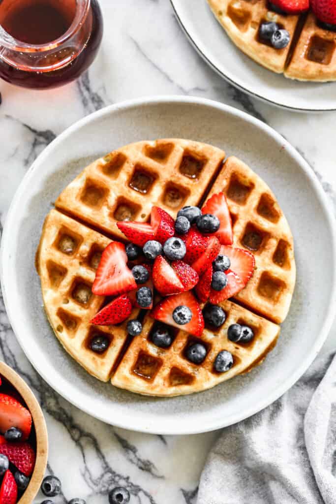 A plate with an overnight Yeasted Waffle topped with fresh strawberries and blueberries.
