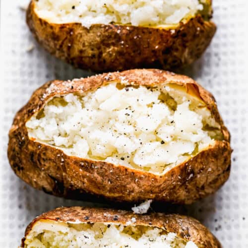 Three quick Air Fryer Baked Potatoes on a platter, split in half and sprinkled with salt and pepper.