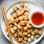 A plate of crispy air fryer tofu with chopsticks and a side of sweet and sour sauce.