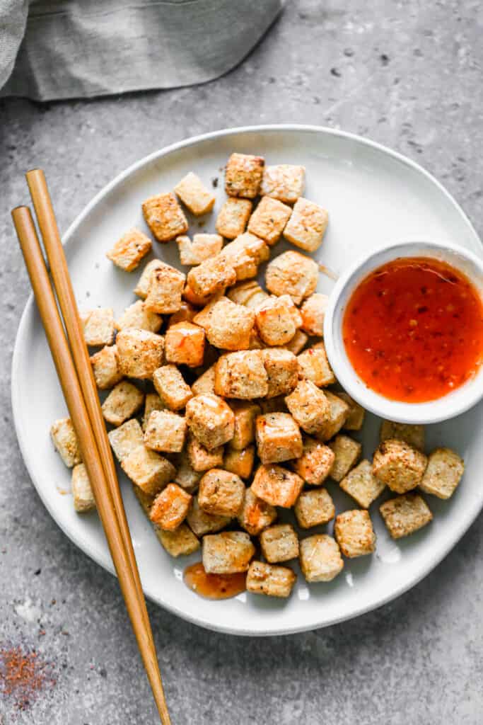 A plate of crispy air fryer tofu with chopsticks and a side of sweet and sour sauce.