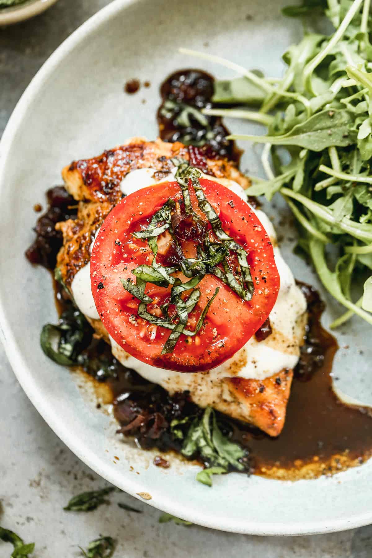 A baked chicken caprese recipe with melted mozzarella cheese and topped with a slice of fresh tomato and chopped basil.
