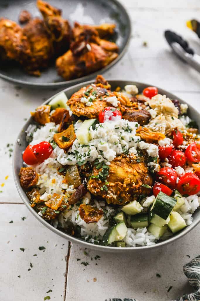 An easy Chicken Shawarma Bowl recipe with a bed of rice and topped with chicken, tomatoes, cucumber, and feta cheese.