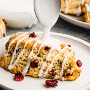 An easy scone recipe with craisins on a plate with glaze being drizzled on top.