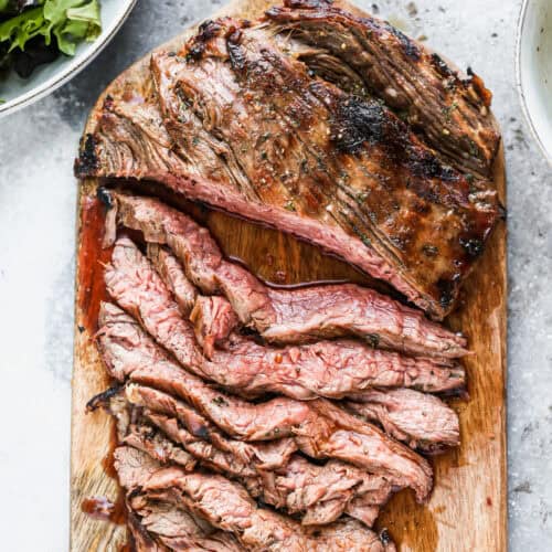 The best Marinated Flank Steak recipe on a cutting board with half of it sliced into thin strips.