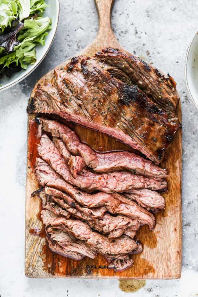 The best Marinated Flank Steak recipe on a cutting board with half of it sliced into thin strips.