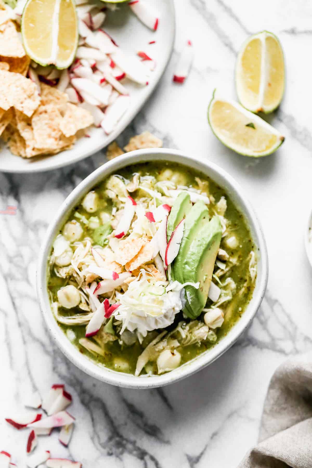 Pozole verde de pollo in a bowl topped with sour cream, crushed tortilla chips, sliced radishes, and avocado. Ready to enjoy!