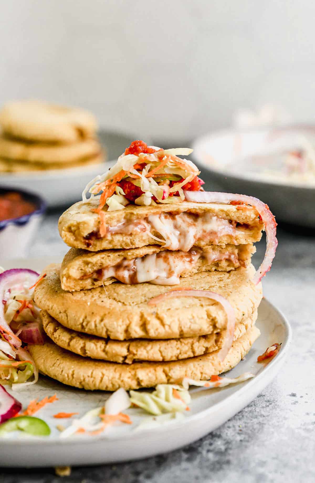 A stack of bean and cheese pupusas with one of them cut in half to show the melted cheese.