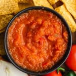 An easy Salsa Roja recipe in a bowl surrounding by veggies and chips.