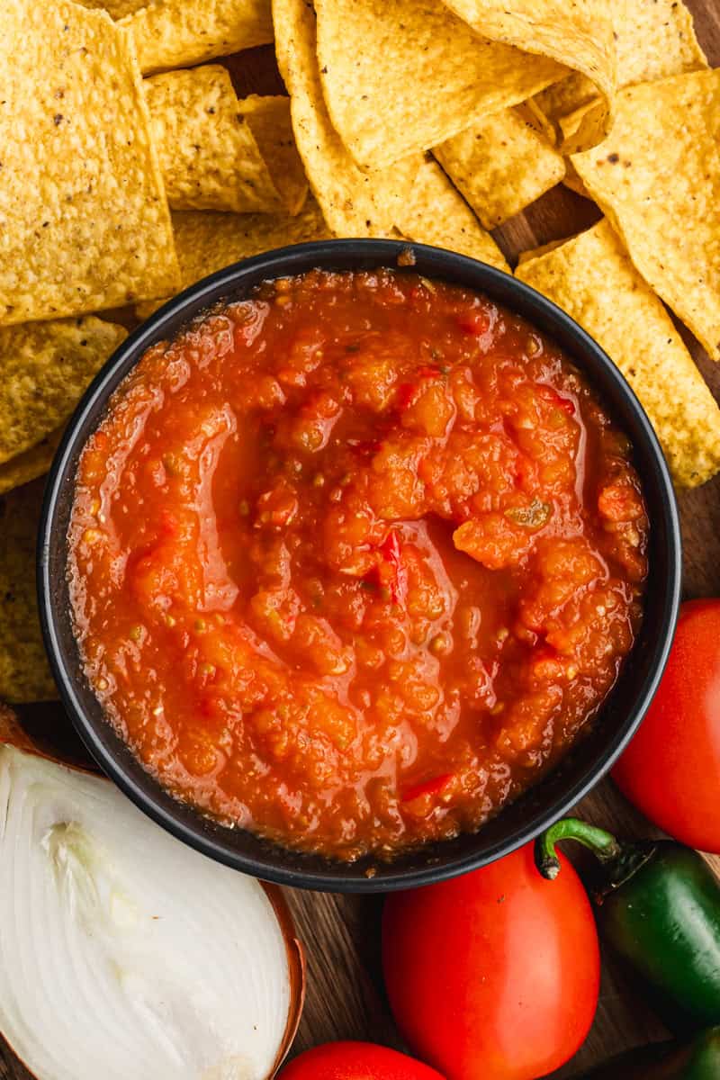 An easy Salsa Roja recipe in a bowl surrounding by veggies and chips. 