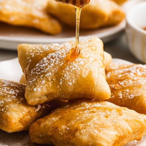 The best Sopapillas on a plate dusted with powdered sugar and drizzled with honey.