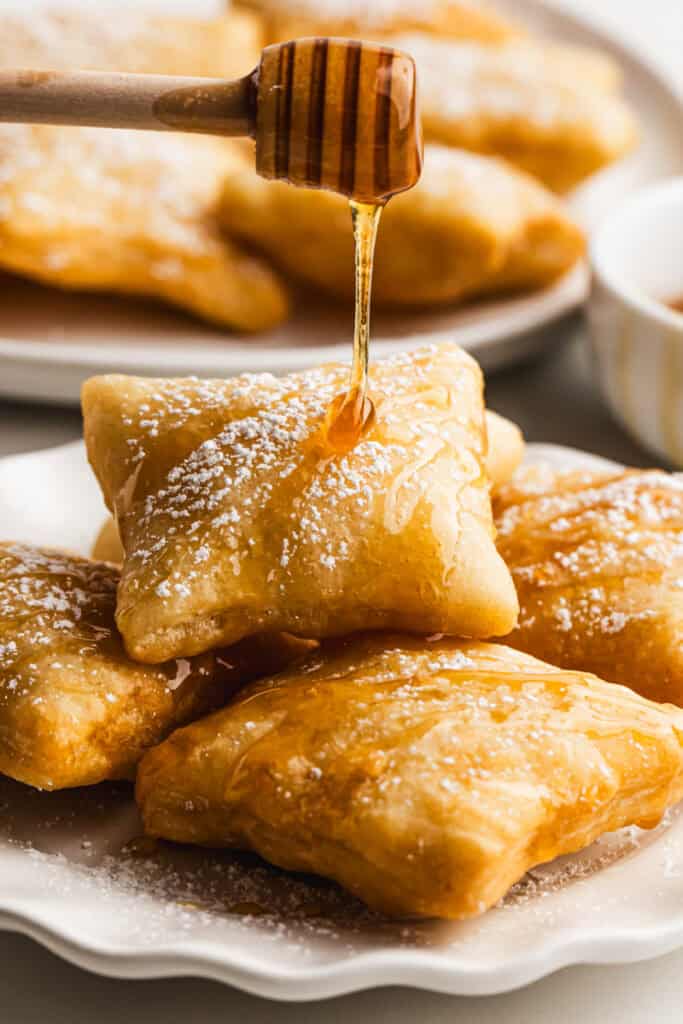 The best Sopapillas on a plate dusted with powdered sugar and drizzled with honey.