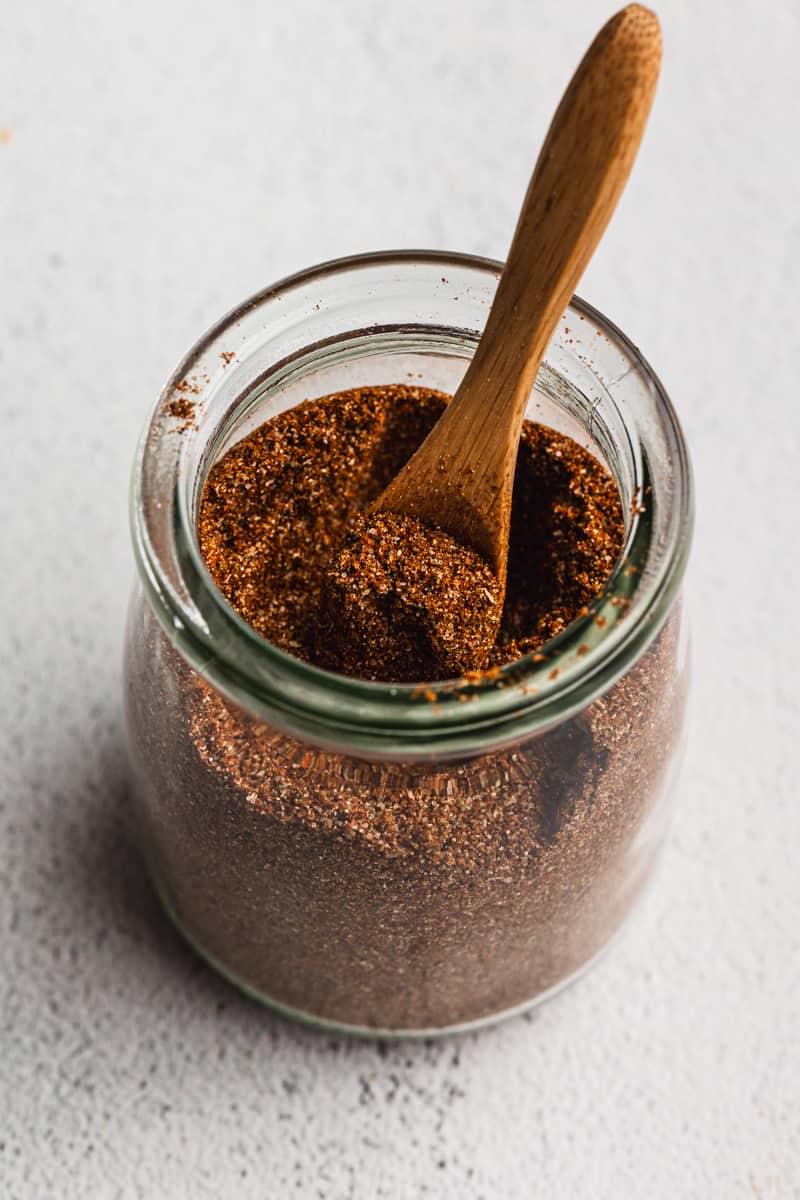 A jar with homemade Taco Seasoning being scooped with a wooden teaspoon.
