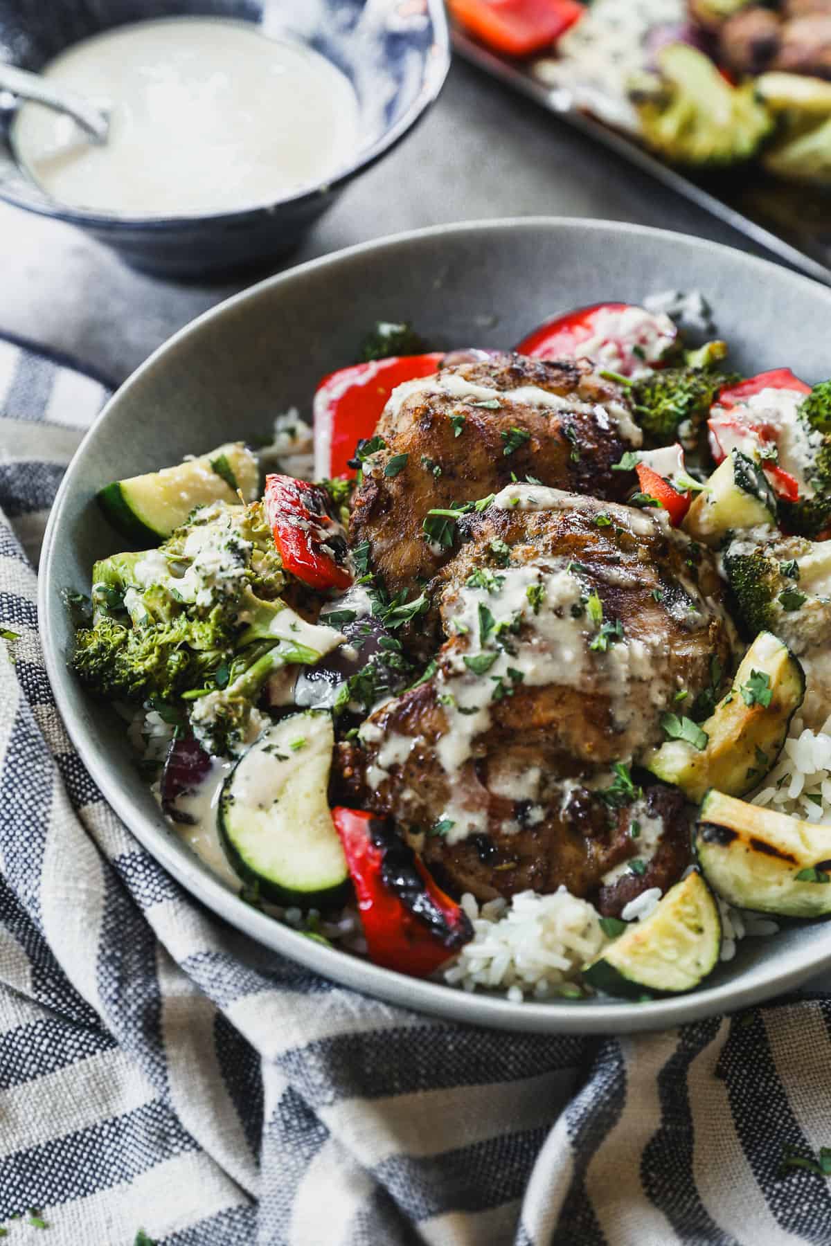 A fresh Tahini Chicken Bowl with grilled chicken thighs and vegetables, drizzled with a homemade sauce.