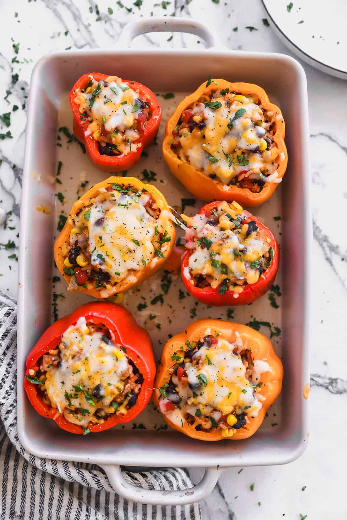 Six homemade vegetarian stuffed peppers with rice, beans, veggies, and topped with cheese. They are out of the oven and ready to eat.