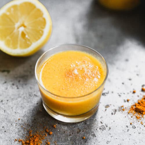 A homemade Ginger Shot recipe in a glass with turmeric dusted on top, ready to enjoy.