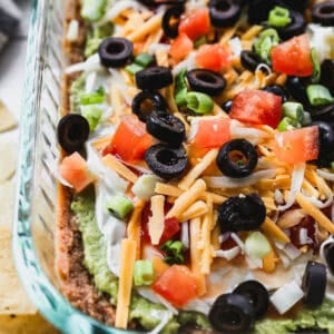 This old fashioned 7 Layer Dip Recipe has layers of beans, avocado, sour cream, cheese, and fresh toppings. It's simple to throw together and an instant hit at any game day or party!