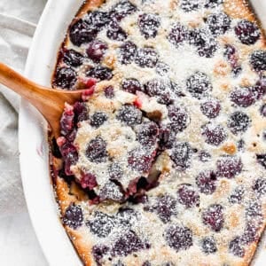 An oval baking dish filled with French Cherry Clafoutis, dusted with powdered sugar and ready to serve.