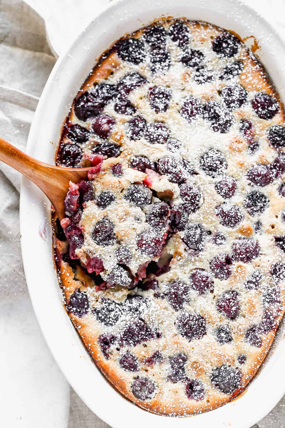 An oval baking dish filled with French Cherry Clafoutis, dusted with powdered sugar and ready to serve.
