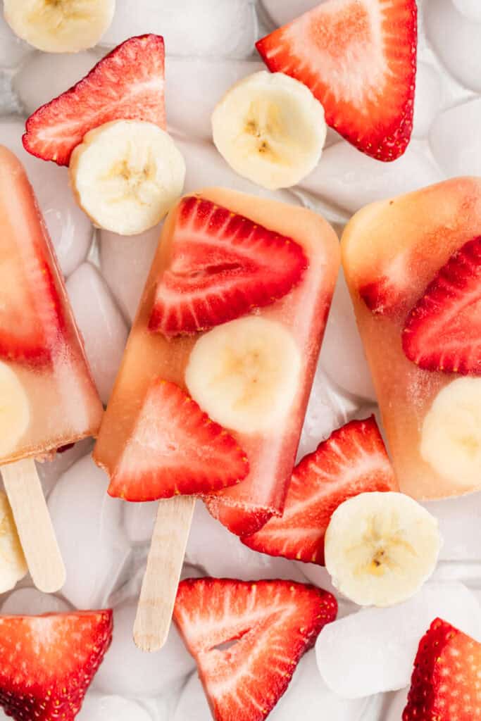 Homemade fruit popsicles made with sliced strawberries, bananas, and apple juice.