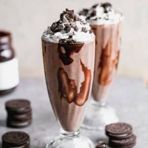 The best Oreo Milkshake recipe served in a tall milkshake glass, topped with whipped cream and crushed Oreos.