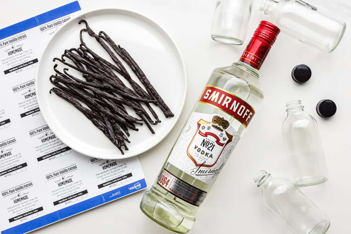 All of the ingredients needed to make Madagascar vanilla extract at home: vanilla beans, vodka, glass bottles, and homemade labels.