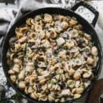 A cast iron pan filled with creamy chicken marsala pasta with sautéed mushrooms, topped with grated parmesan cheese.