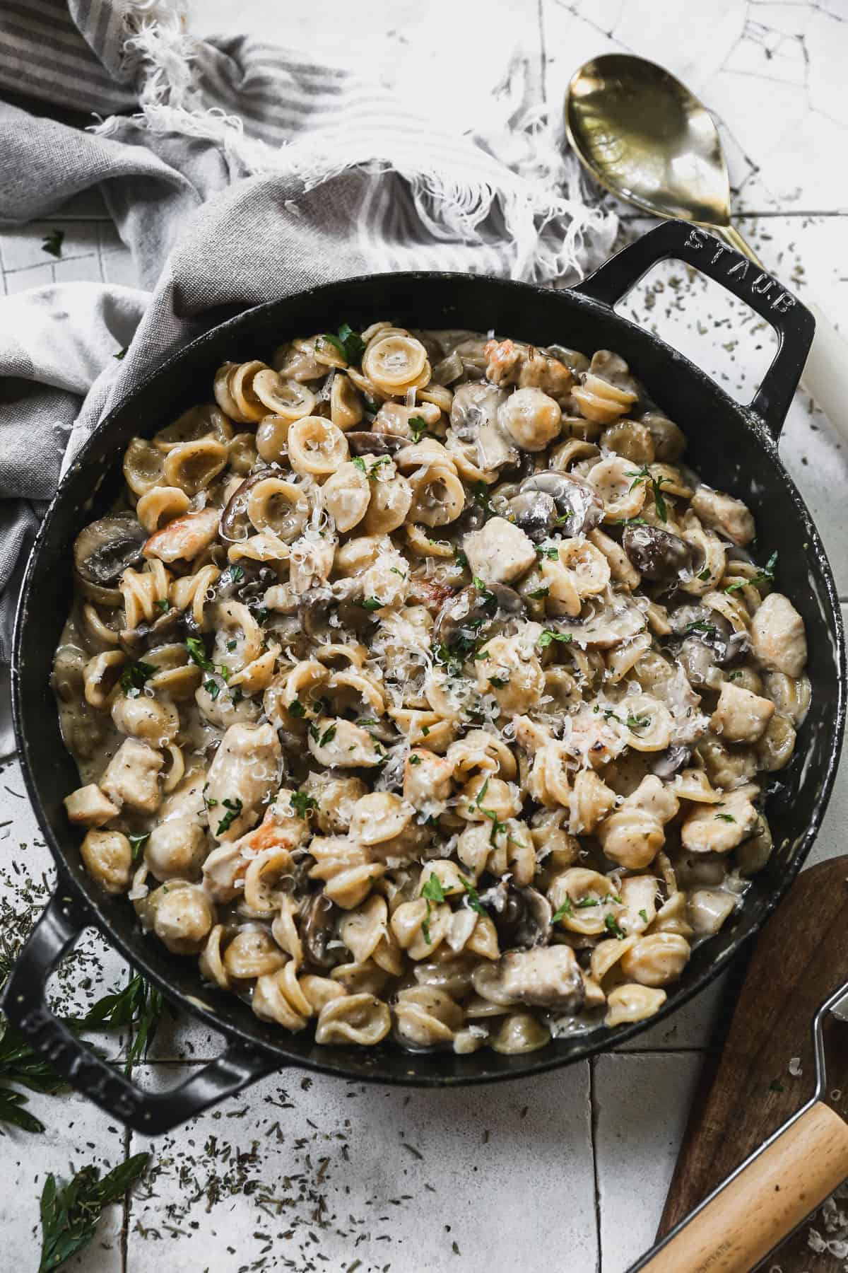 A cast iron pan filled with creamy chicken marsala pasta with sautéed mushrooms, topped with grated parmesan cheese.